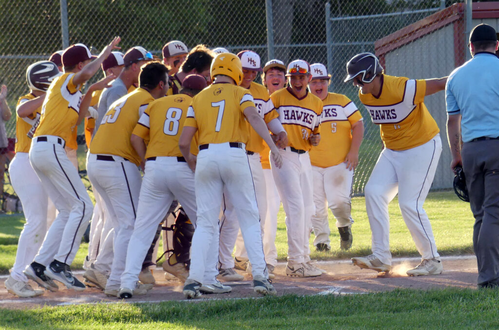 Nick Bronstad is welcomed by his Hawk teammates as he prepares to leap onto home plate after hitting a two-run home run against Trinity Christian.