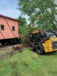 A TASC force volunteer behind the wheel makes short work of removing overgrown plant life at the caboose in City Park.