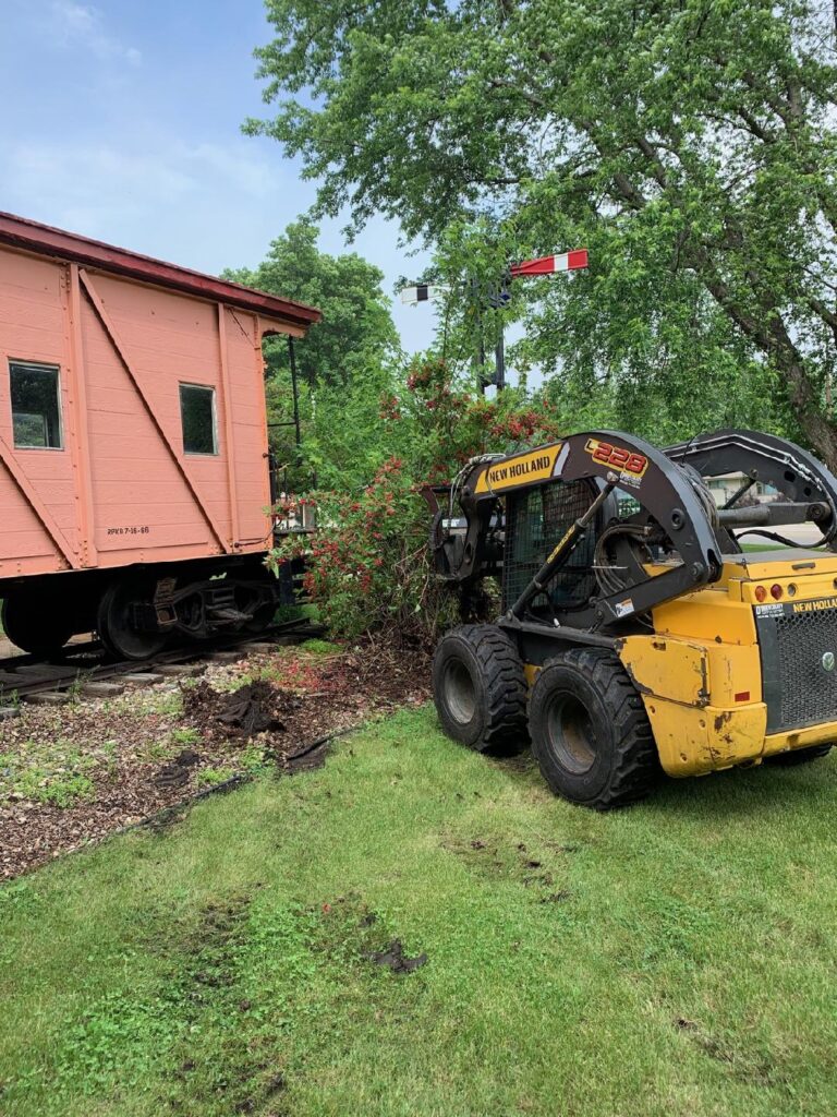 A TASC force volunteer behind the wheel makes short work of removing overgrown plant life at the caboose in City Park.